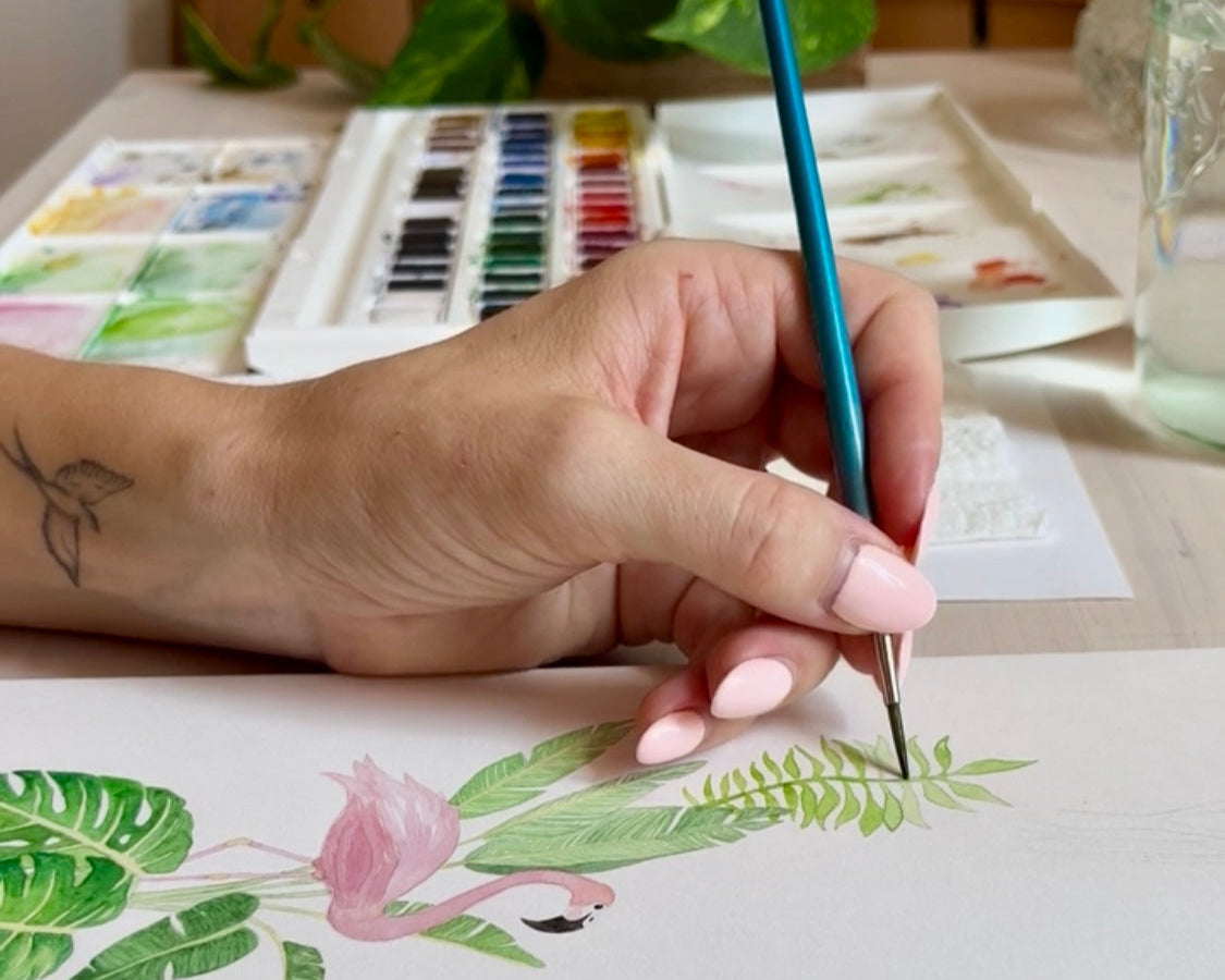 Hand holding paint brush painting green leaves in watercolour on the original painting for the jungle-themed name poster