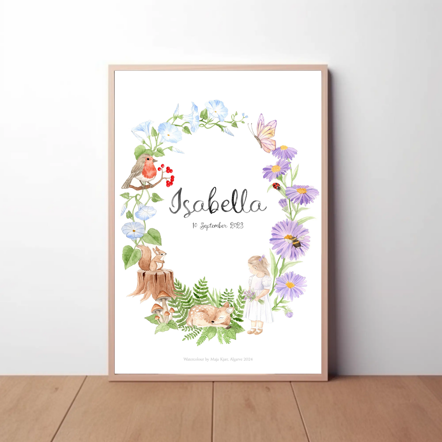 Woodland baby girl name print with animals and flowers in oak frame leaning against wall on wooden floor