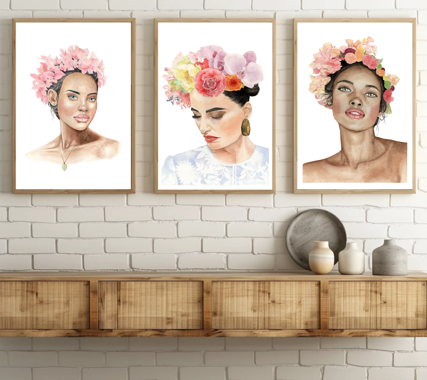 Three watercolour art prints of women with floral headdresses in wooden minimalistic frames hanging on white brick wall above shelf
