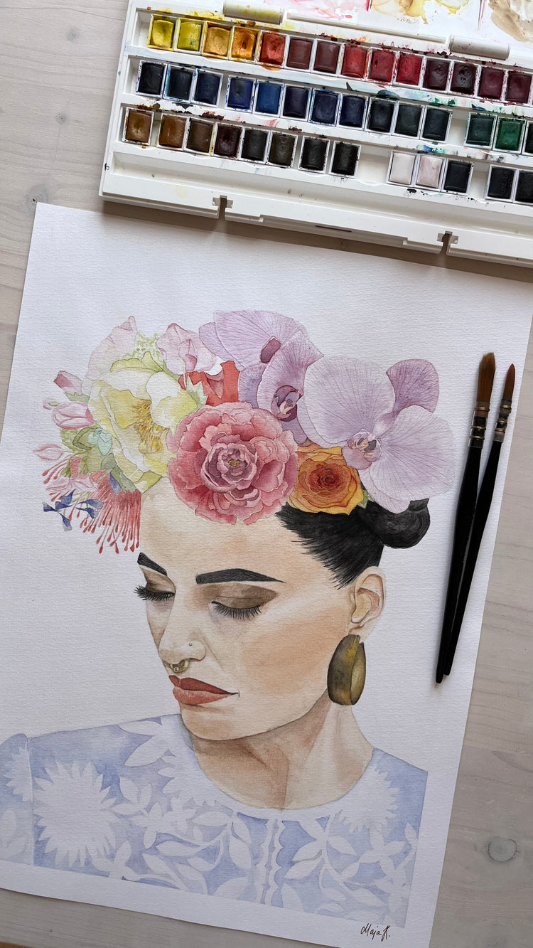 Flat-lay of original watercolour painting of woman with Mexican-inspired floral headdress next to watercolour brushes and watercolours on table