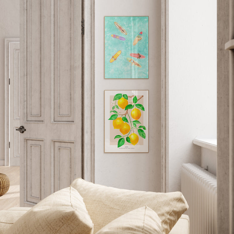 Two art prints with women surfers in an aerial view on colourful longboards on a backdrop of turquoise water, framed on the wall in boho inspired room with green plants