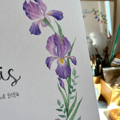 Purple iris flower illustration on a white background with a blurred background of art supplies.