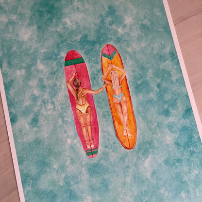 Two women lying on surfboards with a colorful pattern on a textured surface.