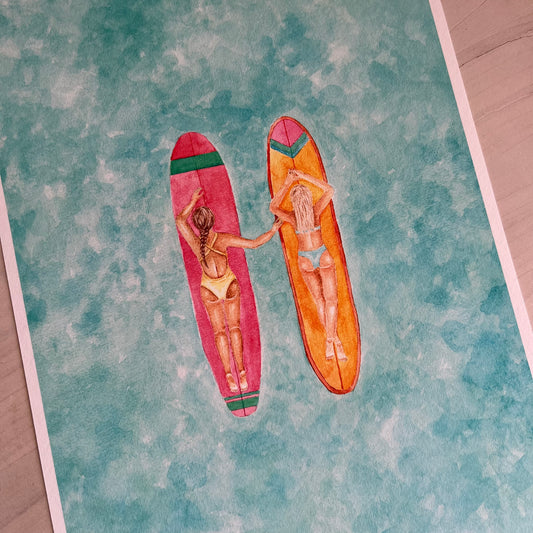 Two women lying on surfboards with a colorful pattern on a textured surface.