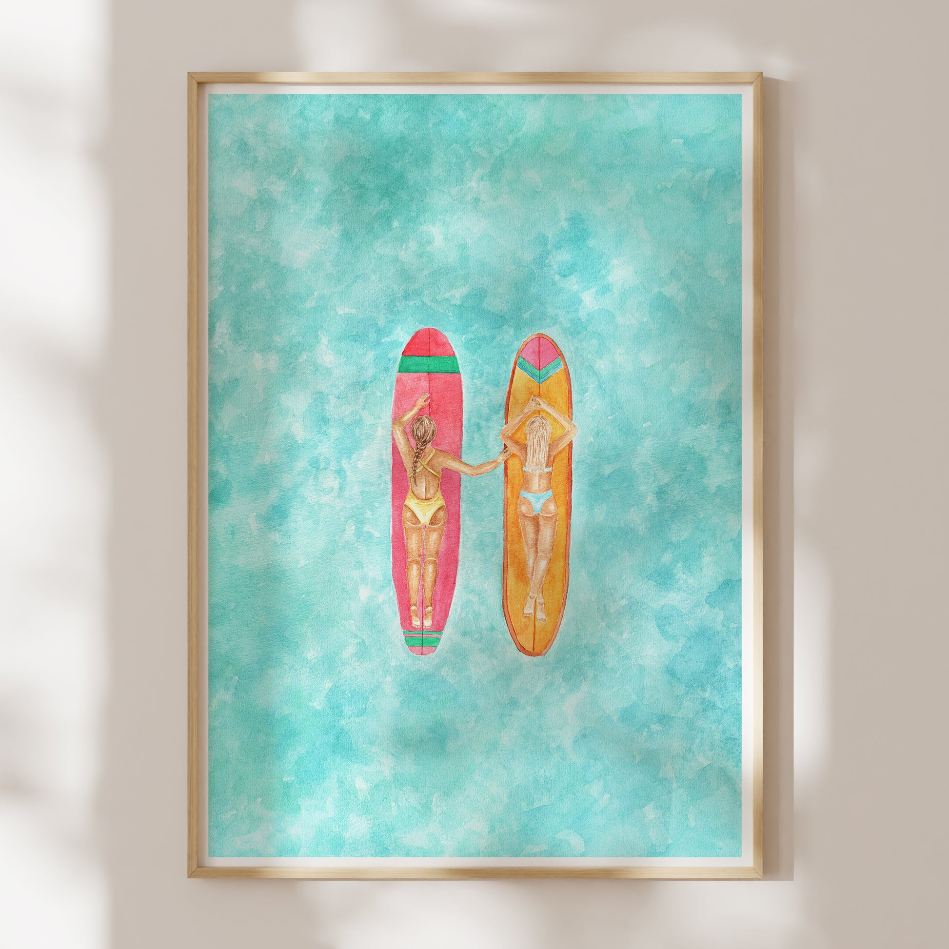 Framed artwork of two women on surfboards against a turquoise background