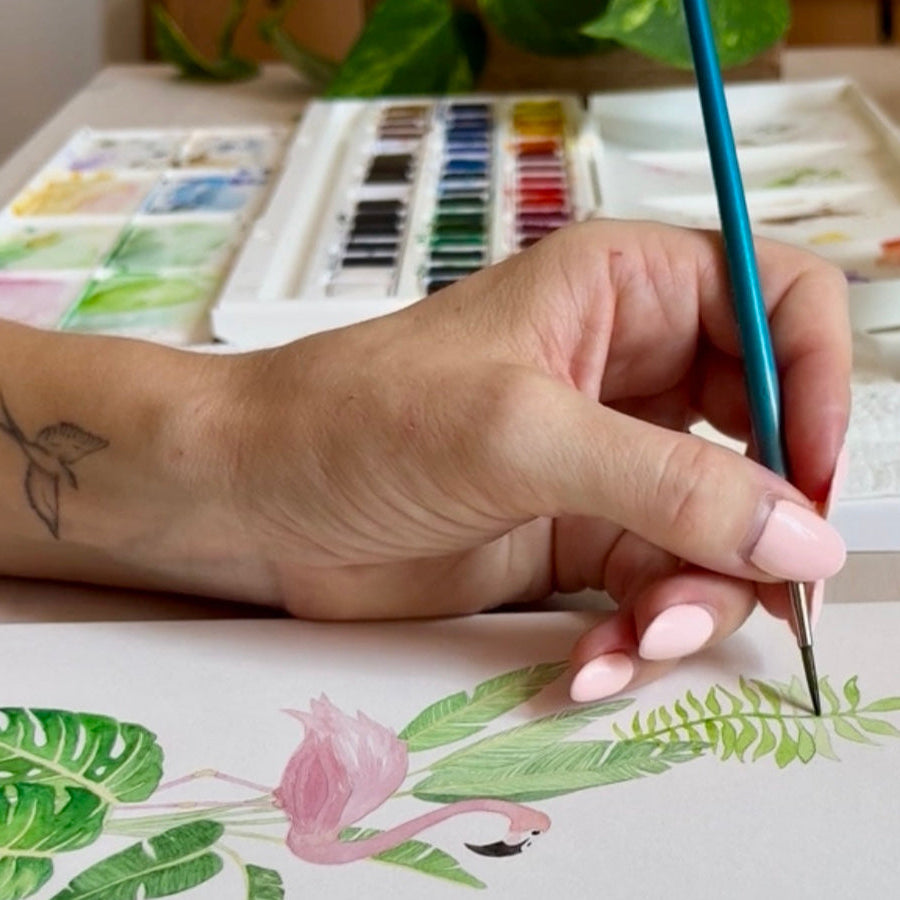 Hand holding paint brush painting green leaves in watercolour on the original painting for the jungle-themed name poster 