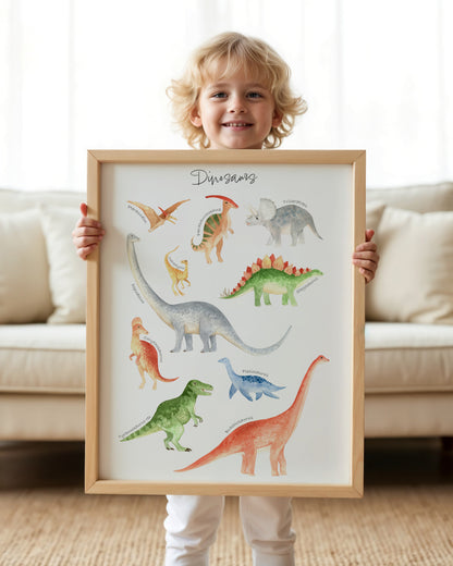 A smiling young child stands indoors holding a framed watercolor dinosaur poster. The poster shows multiple colorful dinosaurs on a white background with the word 'Dinosaurs' at the top.