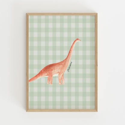 A framed art print featuring a watercolor illustration of a long-necked dinosaur on a light green and white gingham checkered background, housed in a light natural wood frame.