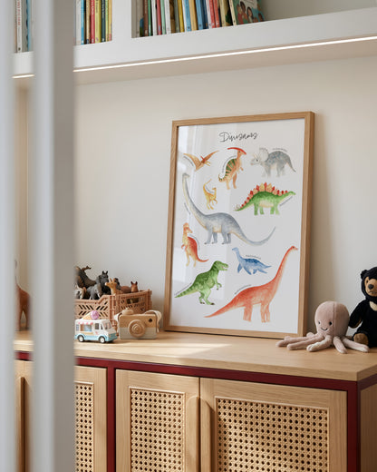 A framed watercolor dinosaur art print with a light wood frame, leaning on a wooden children's cabinet in a styled nursery or playroom setting.