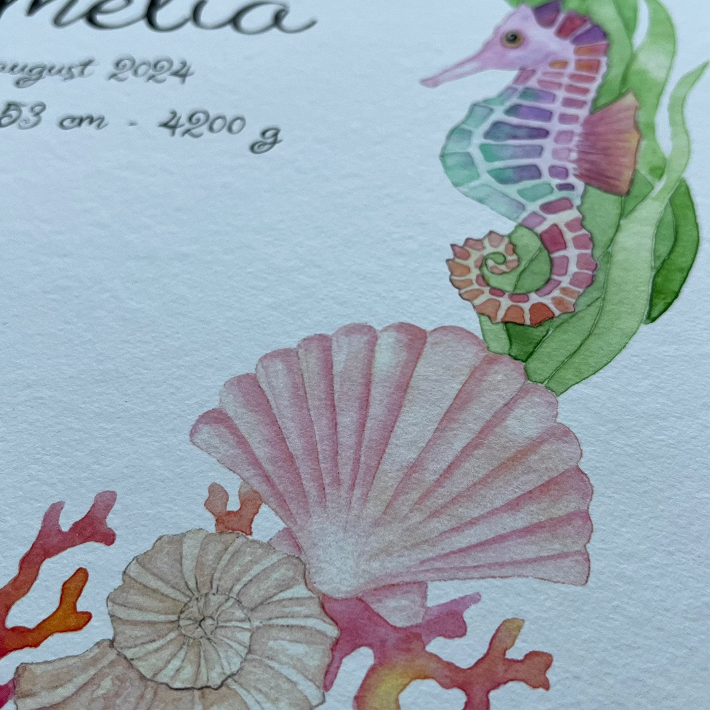 A close-up of a watercolor print featuring an underwater sea life design with a seahorse, shells, coral, and starfish around printed text including the name 'Amelia' and birth details.