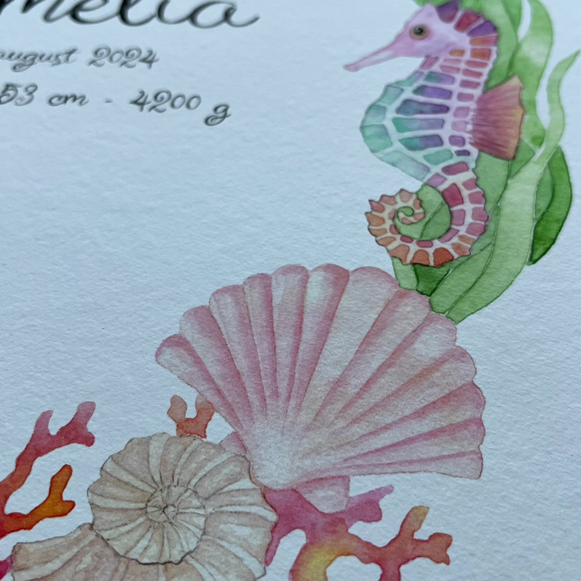 A close-up of a watercolor print featuring an underwater sea life design with a seahorse, shells, coral, and starfish around printed text including the name 'Amelia' and birth details.