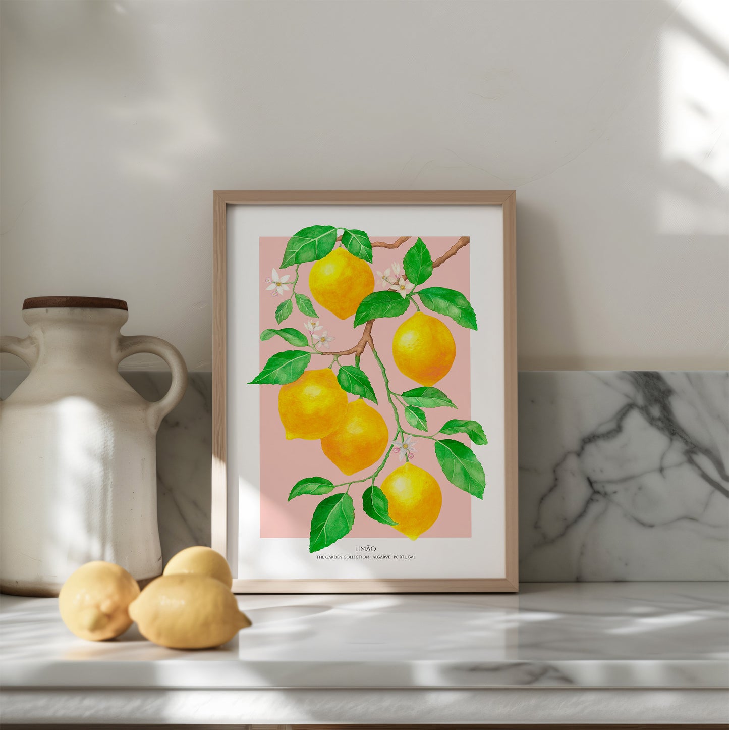 Framed artwork of lemons on a pink background on a shelf with a vase and lemons.