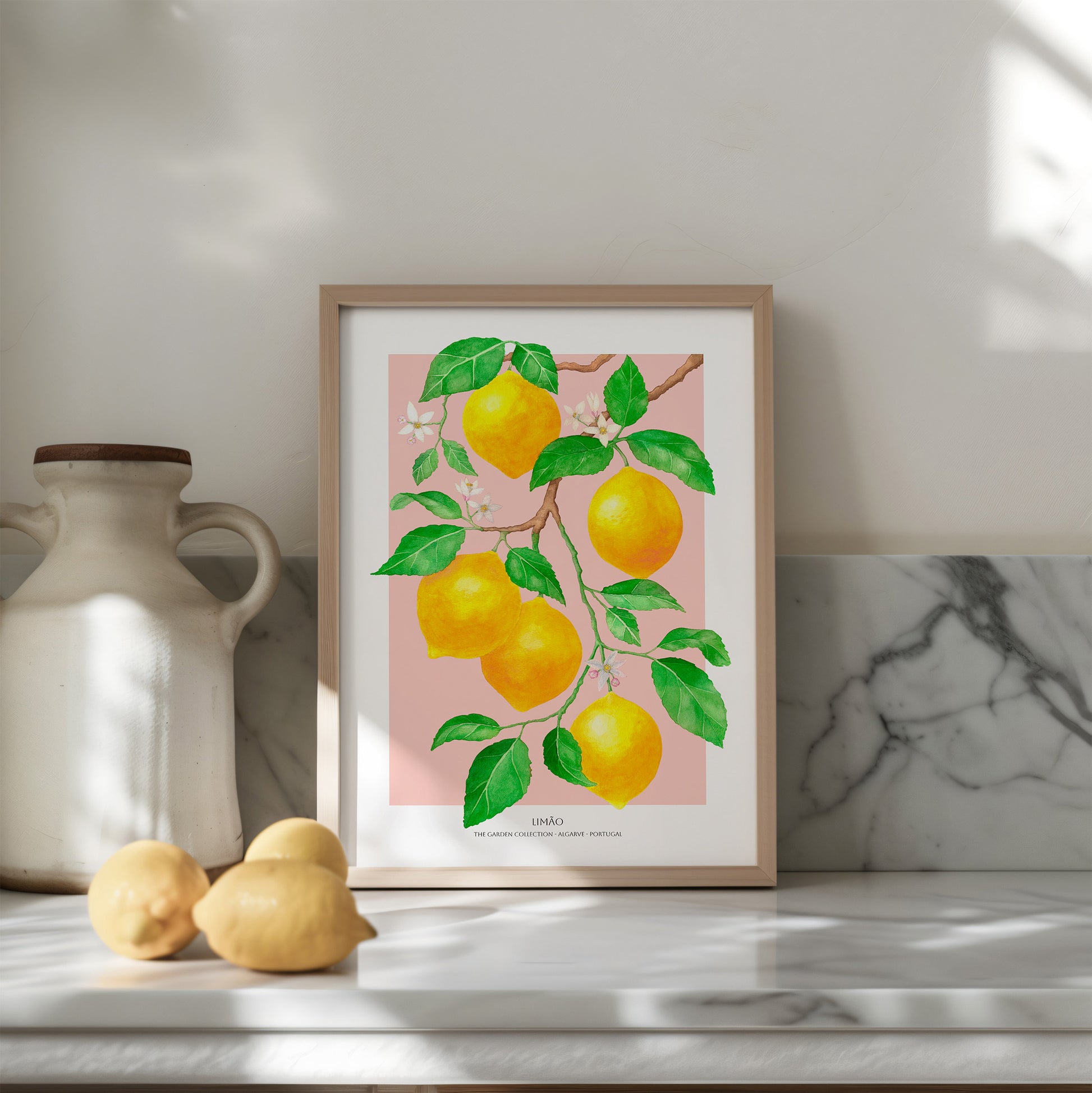 Framed artwork of lemons on a pink background on a shelf with a vase and lemons.