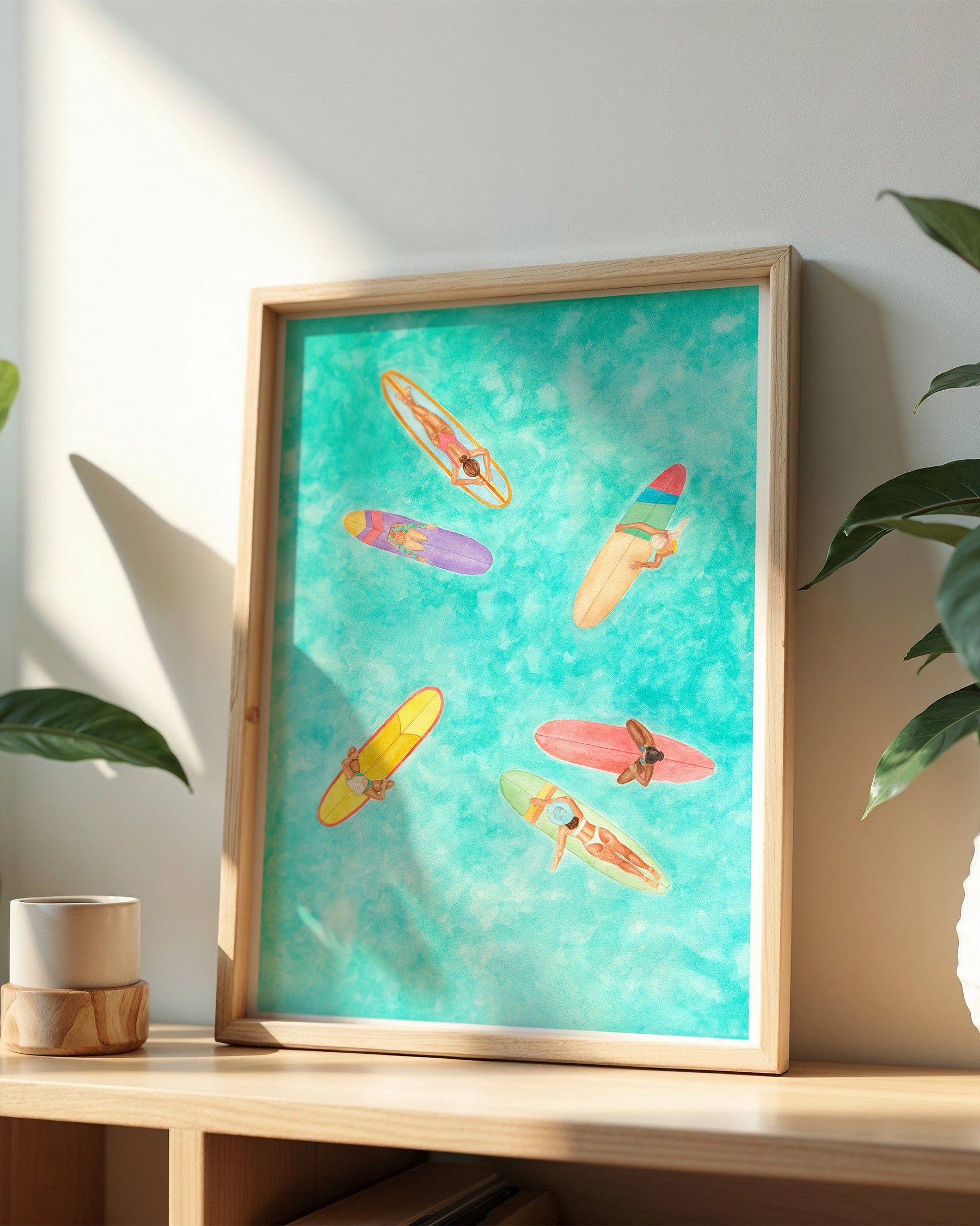 Framed artwork of colorful surfboards on a teal background, displayed on a shelf with plants.