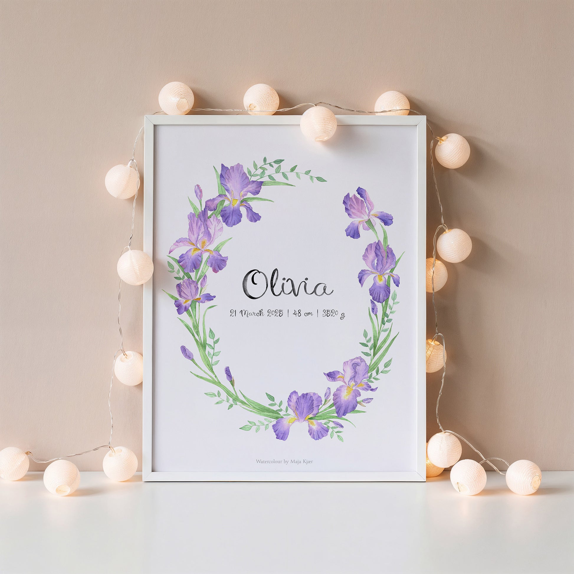 Framed print with purple floral design and 'Olivia' text, surrounded by string lights on a beige wall.