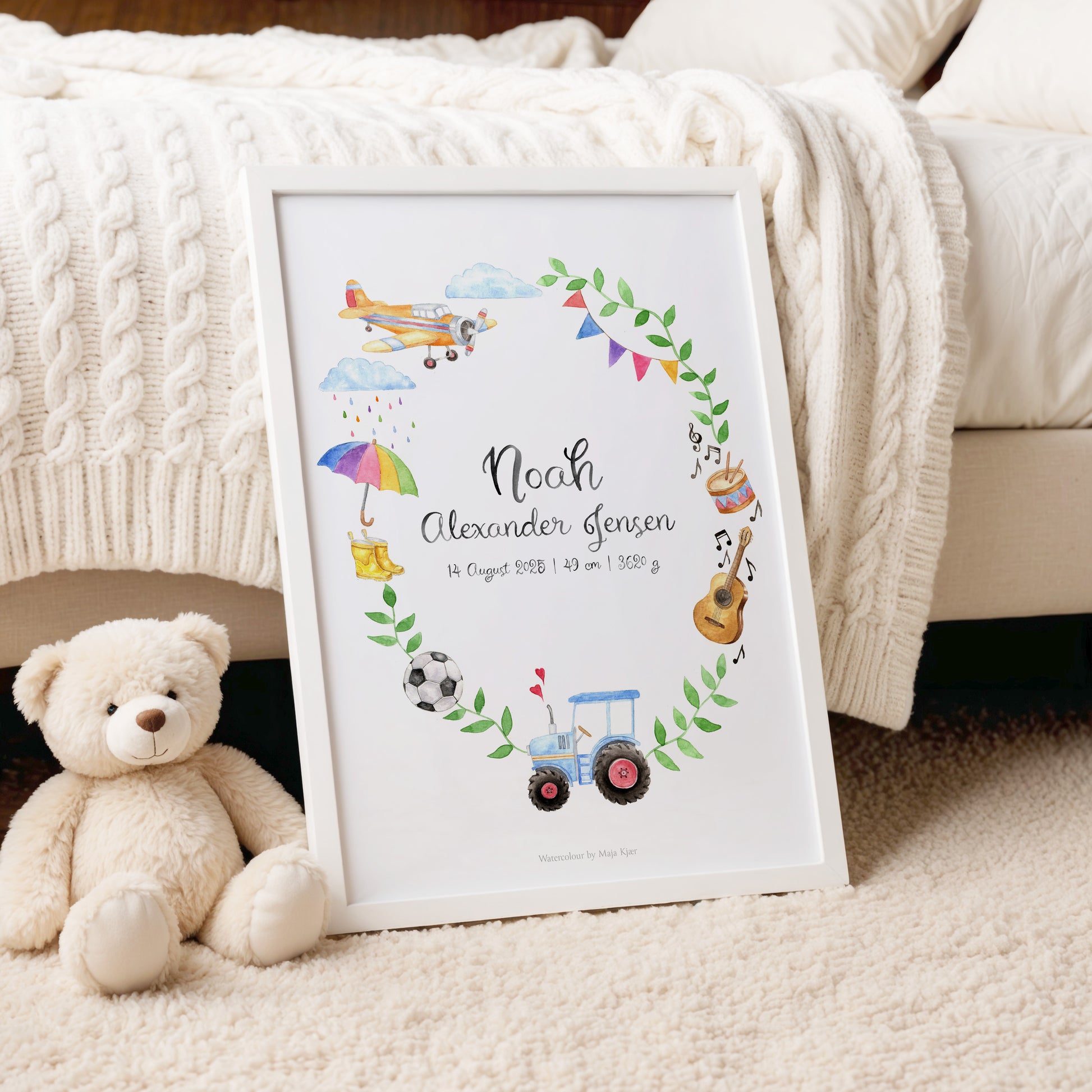 Framed baby milestone chart with illustrations of toys and text, placed on a carpeted floor with a teddy bear beside it.