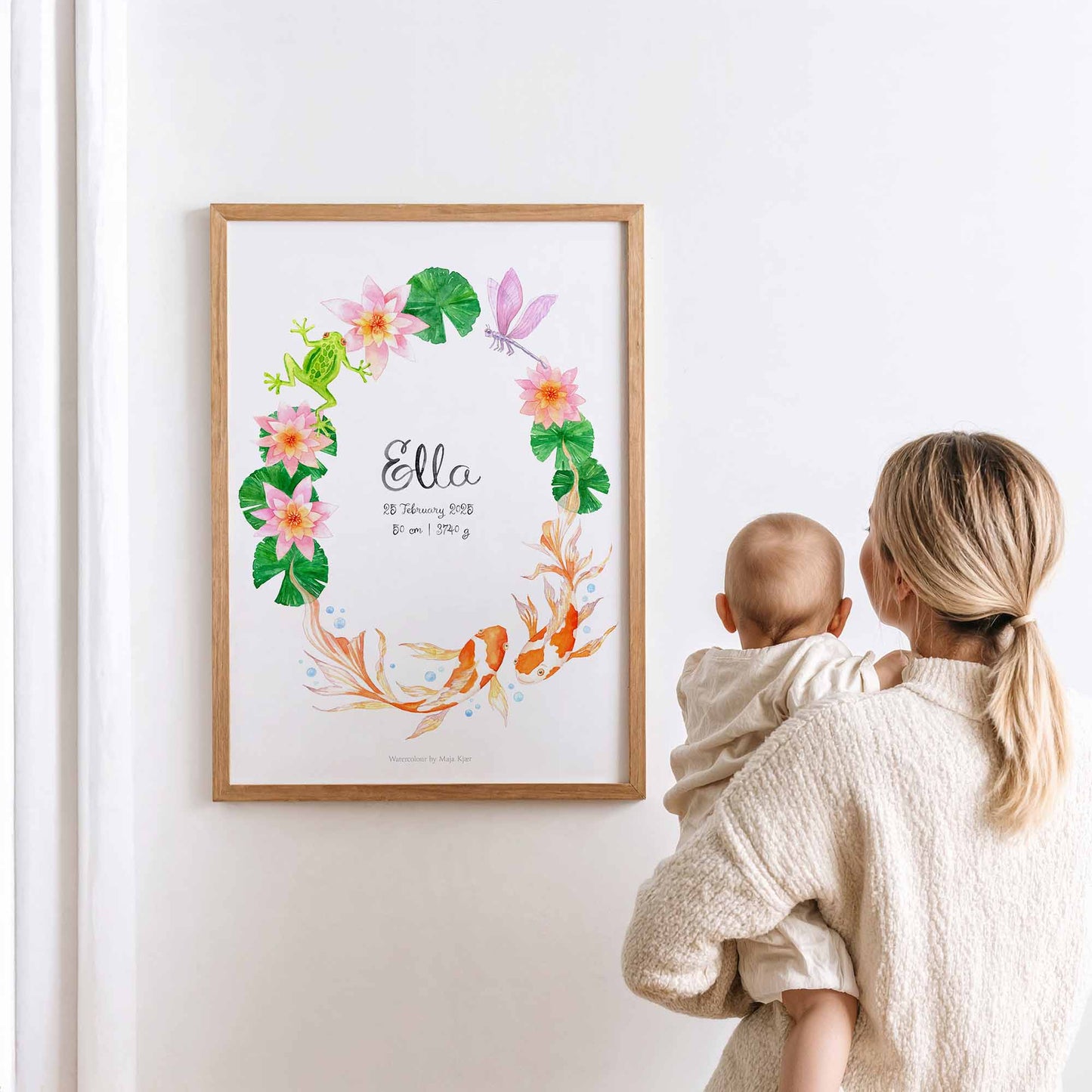 Woman holding a baby looking at a framed watercolour poster with baby's name and birth details for the zodiac sign Pisces 