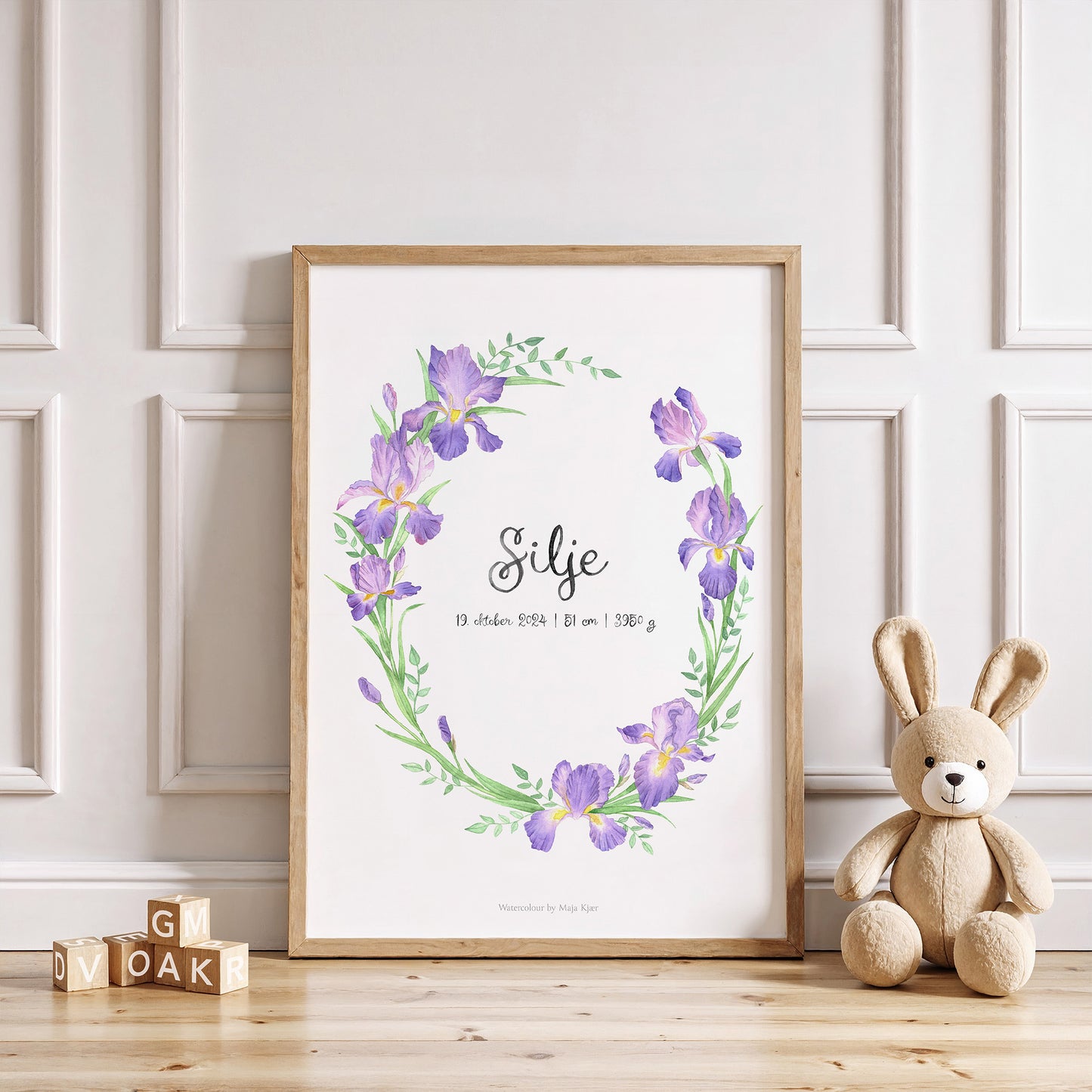 Framed floral print with a teddy bear and wooden blocks on a light wood floor.
