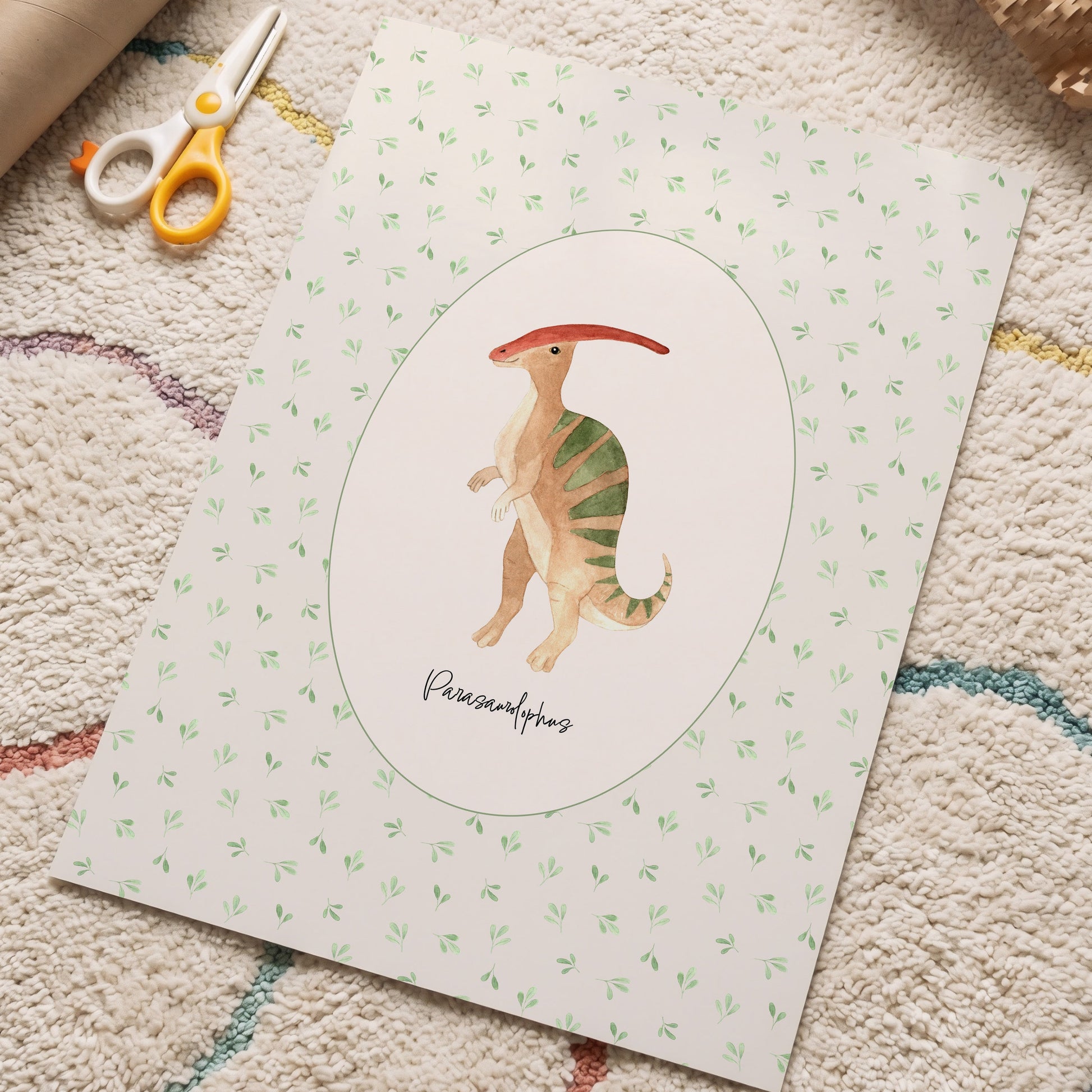 A square art print featuring a painted Parasaurolophus dinosaur in the center, surrounded by a white oval and a light green patterned border. The print is styled on a textured beige rug with craft scissors and a cardboard tube nearby.