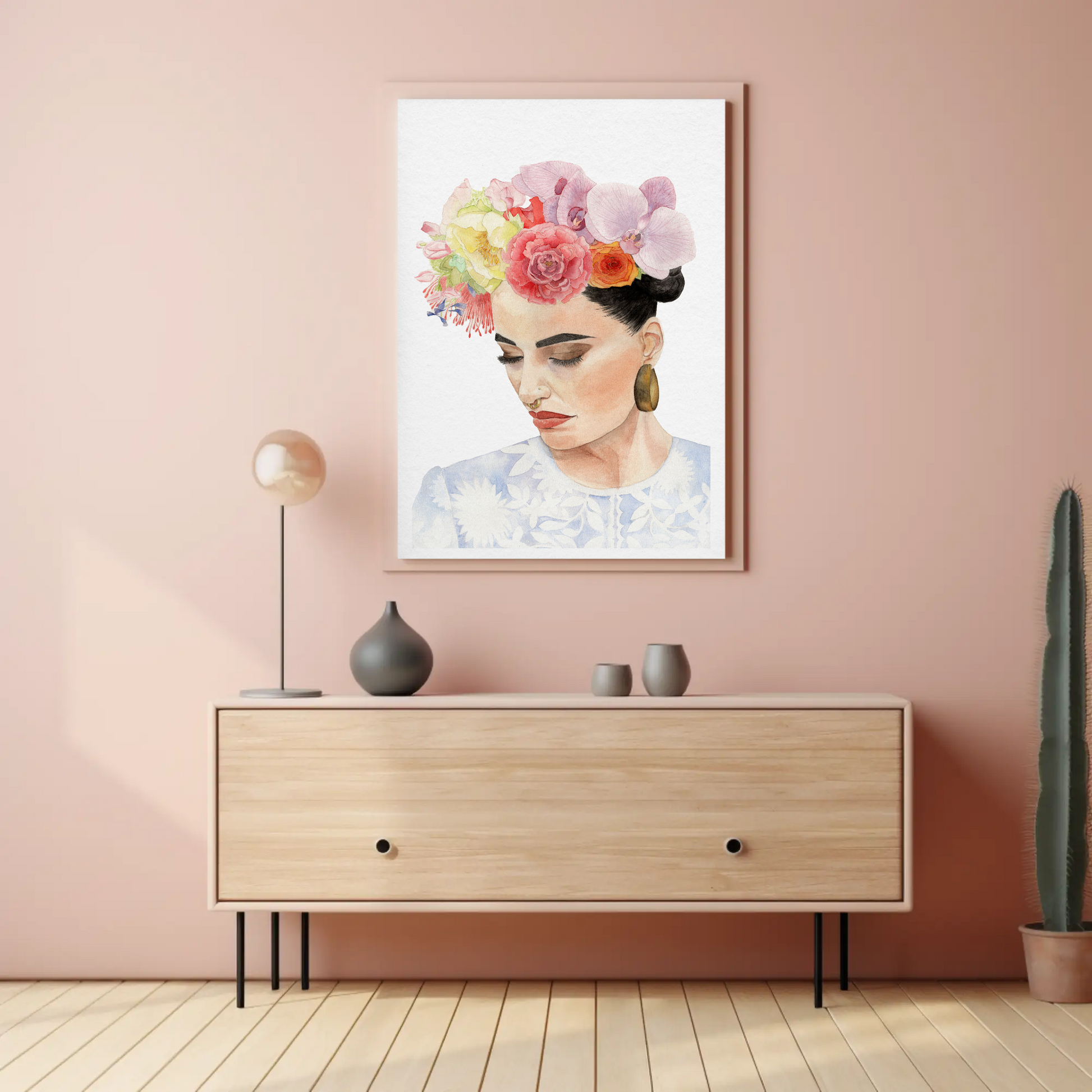 Framed watercolour portrait of woman with flower headdress inspired by Frida Kahlo hanging on warm pink wall in living room