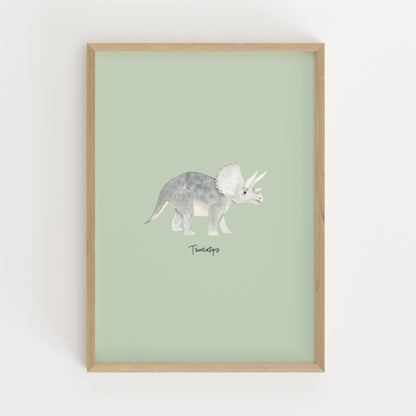A framed art print featuring a watercolor illustration of a Triceratops dinosaur on a pale sage green background, enclosed in a light natural wood frame and mounted on a white wall.