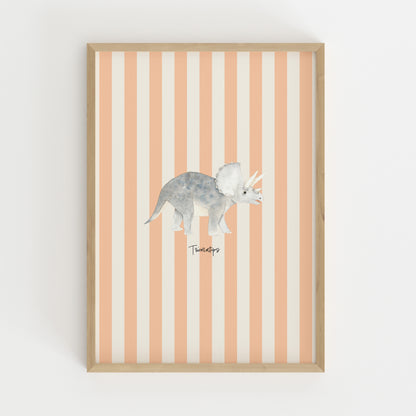 A framed wall art print featuring a watercolor-style gray Triceratops dinosaur centered on vertical peach and off-white stripes, set in a light natural wood frame against a white wall.