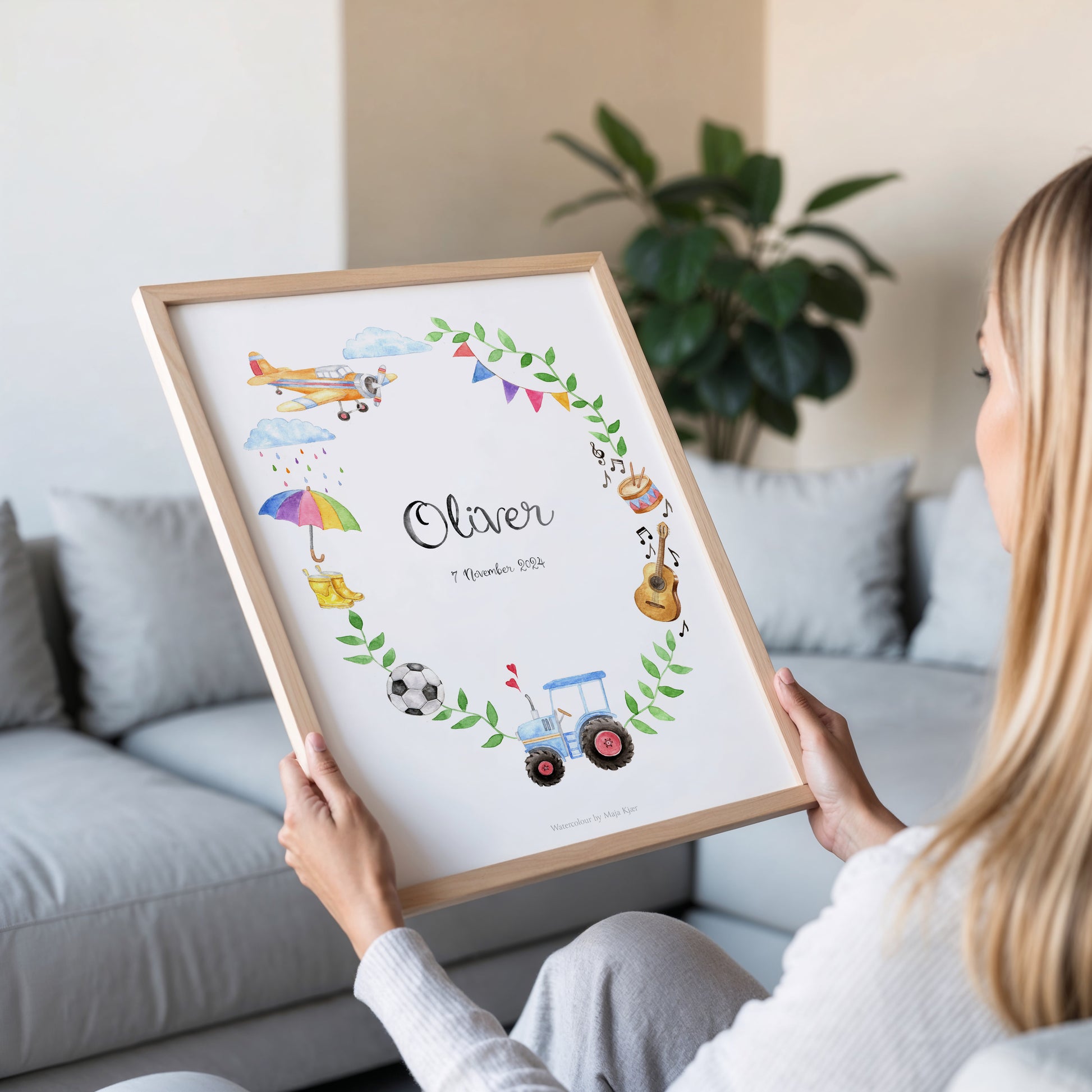 Person holding a framed children's name art print with illustrations of toys and objects.